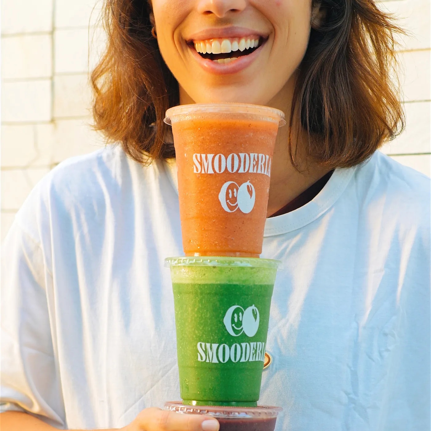 Cliente sorrindo com quatro copos de smoothie empilhados nos braços